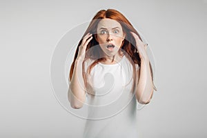 Redhead girl on white background with strong expression of fear, round eyes