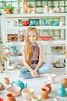 Girl wih many cups made from clay sitting in pottery studio