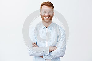Redhead guy knows everything about business, standing in trendy shirt over gray wall with crossed hands on chest