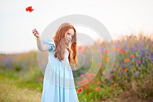 Redhead kid girl playing with wild flowers at summer day outdoor