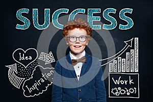 Redhead little boy in glasses and suit against hand drawing sketch and success text. Business idea and success concept
