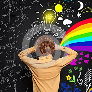 Redhead little boy thinking and standing near blackboard with many question marks, lightbulb, science and arts pattern