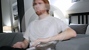 Redhead man comes and sits on sofa in bedrrom