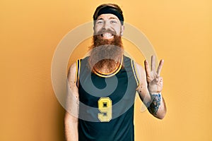 Redhead man with long beard wearing basketball uniform showing and pointing up with fingers number three while smiling confident