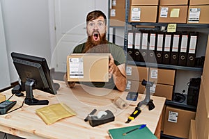 Redhead man with long beard working at small business ecommerce afraid and shocked with surprise and amazed expression, fear and