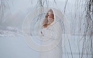 Redhead mature woman in her fifties with red curly hair and white hooded coat freezes in the snowy winter landscape