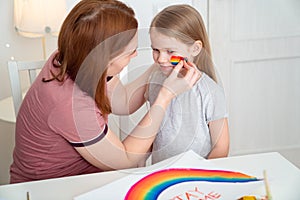 Mom draws daughter of rainbow on cheek. stay home. photo