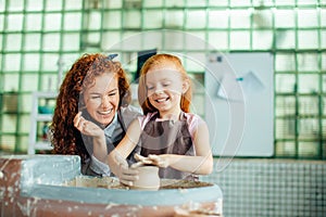 Redhead mother and her child daughter moulding with clay on pottery wheel