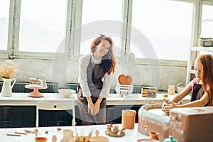 Redhead mother and her child daughter moulding with clay on pottery wheel