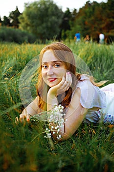 Redhead portrait of a beautiful young sexy red-haired woman, lying in the spring sun, relaxing on the green grass.