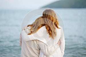 Redhead senior mother and her adult beautiful daughter are walking together on the sea shore