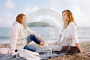A redhead senior mother and her adult pregnant daughter are having a picnic by the sea shore. Happy meeting of a mother and her photo