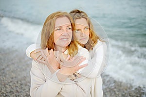 Redhead senior mother and her beautiful adult daughter are walking together and embracing. Family relationships between adult