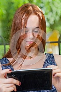 Redhead student leaning against a tree using her tablet on college campus