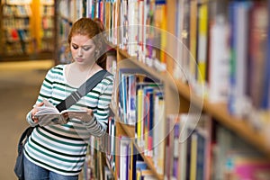 Redhead student reading book leaning on shelf in library photo