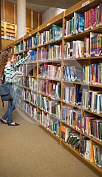 Redhead student taking a book from bookshelf in the library