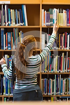 Redhead student taking book from shelf in library