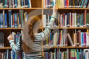 Redhead student taking book from top shelf in library