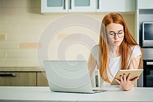 Redhead using the tablet pc and laptop in kitchen