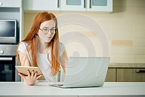 Redhead using the tablet pc and laptop in kitchen