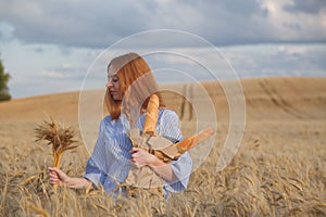 Redhead woman with bakery products in ripe wheat field