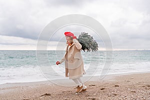 Redhead woman Christmas tree sea. Christmas portrait of a happy redhead woman walking along the beach and holding a