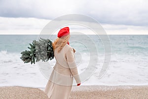 Redhead woman Christmas tree sea. Christmas portrait of a happy redhead woman walking along the beach and holding a