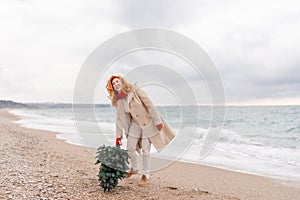 Redhead woman Christmas tree sea. Christmas portrait of a happy redhead woman walking along the beach and holding a