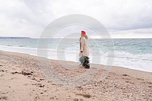 Redhead woman Christmas tree sea. Christmas portrait of a happy redhead woman walking along the beach and holding a