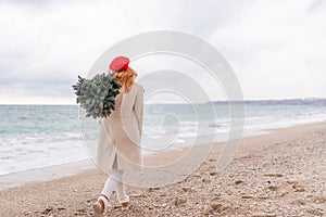 Redhead woman Christmas tree sea. Christmas portrait of a happy redhead woman walking along the beach and holding a