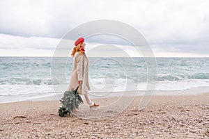 Redhead woman Christmas tree sea. Christmas portrait of a happy redhead woman walking along the beach and holding a