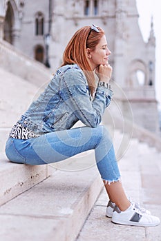 Redhead woman with closed eyes sitting and relaxing on strairs in city