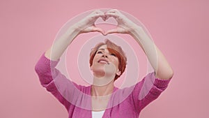 Redhead woman in her 40s making heart shape with hands. Isolated on purple background