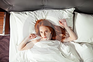Redhead woman lies in bed and looking camera. top view