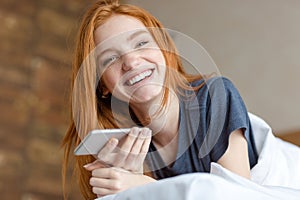 Redhead woman lying on the bed with smartphone