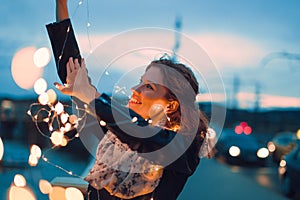 Redhead woman playing with fairy lights outdoors and smile at evening, teal and orange style photo