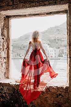 Redhead Woman in Red Dress posing in abandoned house. Curly redhead young caucasian Beautiful Girl in Long flying Cloth