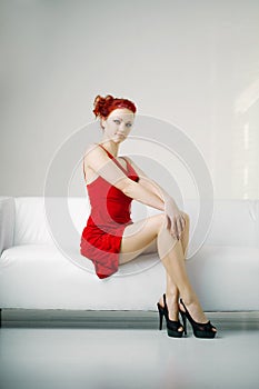 Redhead woman in a red dress on white couch