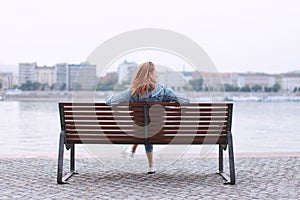 Redhead woman sitting on bench at riverbank back view