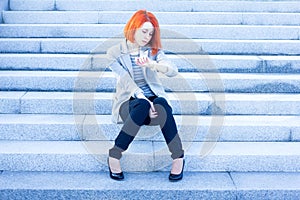Redhead woman sitting outside on the stairs and watching time