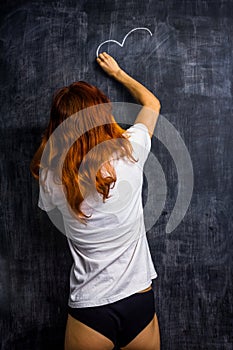 Redhead woman in underwear drawing on a blackboard