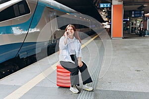 Redhead woman waiting train and using smart phone. Railroad transport concept, Traveler. 30s Middle age woman sitting on