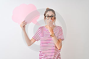 Redhead woman wearing glasses holding cloud speech bubble over isolated white background cover mouth with hand shocked with shame