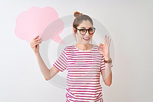 Redhead woman wearing glasses holding cloud speech bubble over isolated white background doing ok sign with fingers, excellent