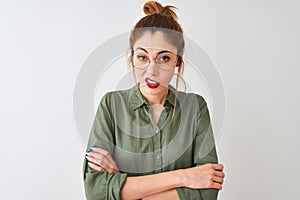 Redhead woman wearing green shirt and glasses standing over isolated white background skeptic and nervous, disapproving expression