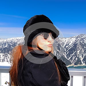 Redhead woman wearing winter clothes in front of a beautiful mountain landscape in the alps of Japan looking back at the camera