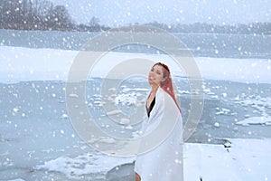 Redhead woman wrapped in towel with happy smile enjoying cold therapy, hardening on snow and ice bath