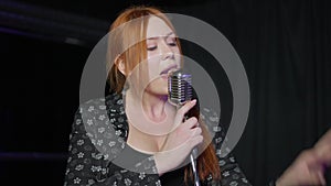 Redhead young Caucasian talented woman singing with microphone performing on stage indoors. Portrait of confident