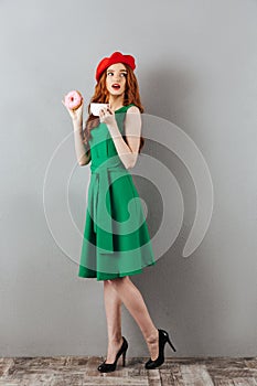 Redhead young cute lady eating donut and drinking coffee.