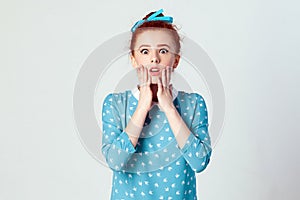 Redhead young girl touching her cheeks and looking at camera with shocked face.